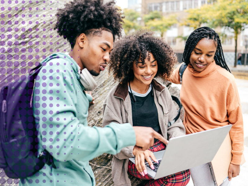 Three young people gather around a laptop outside